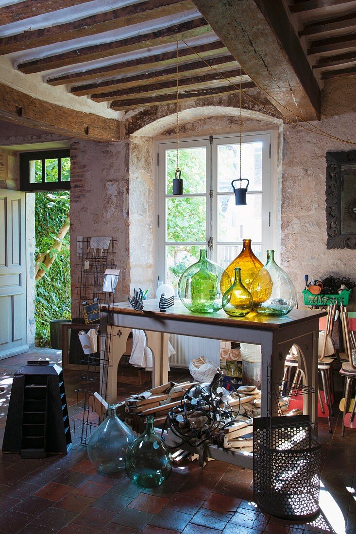 Demijohns of various colours on table in rustic interior with wood-beamed ceiling