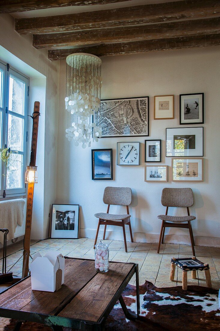 Rustikaler Couchtisch auf Tierfell, im Hintergrund Retro Stühle unter Bildergalerie, in ländlichem Wohnraum
