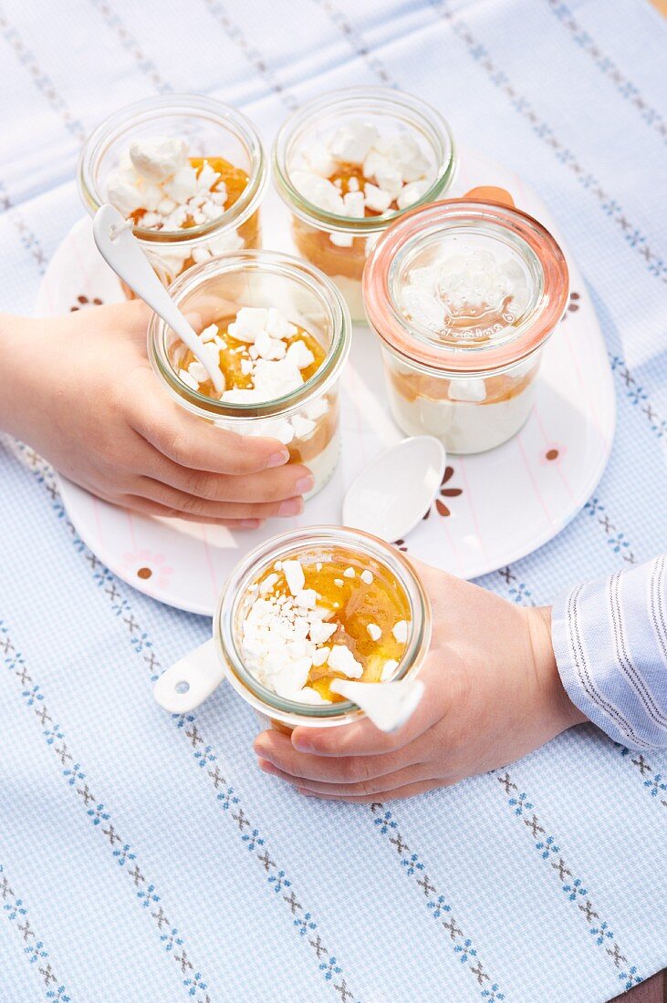 Kinder halten zwei Gläser Eton Mess mit Aprikosen