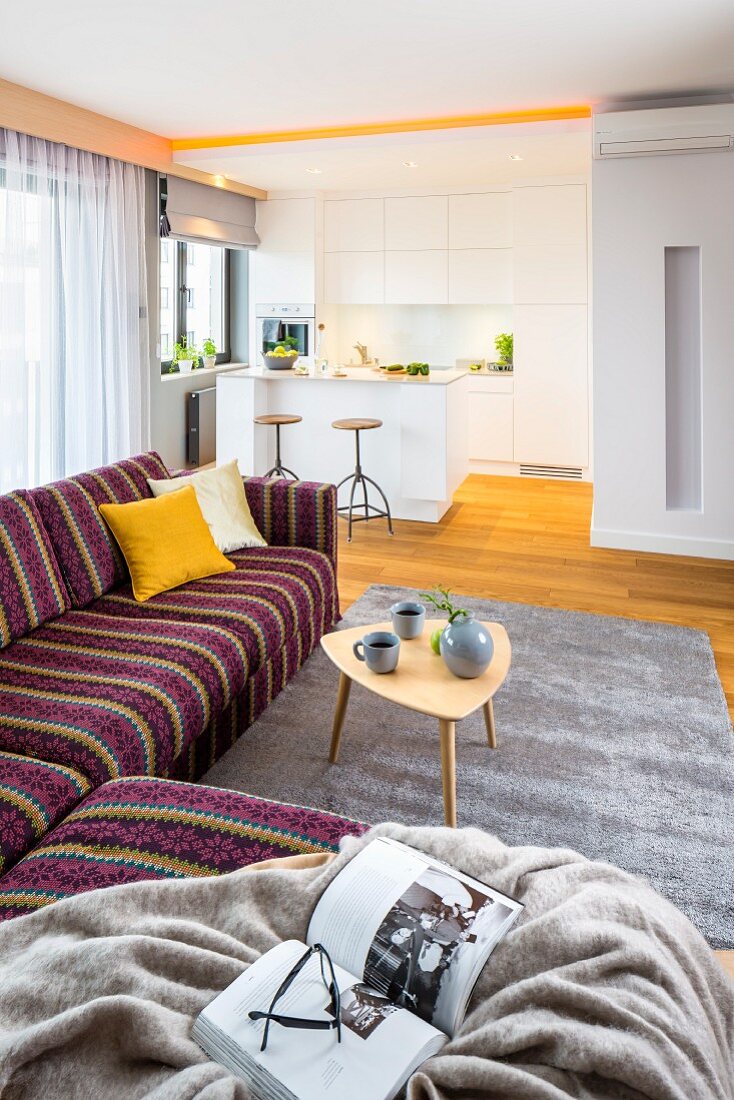 Striped corner sofa and retro side table in front of white kitchen with breakfast bar