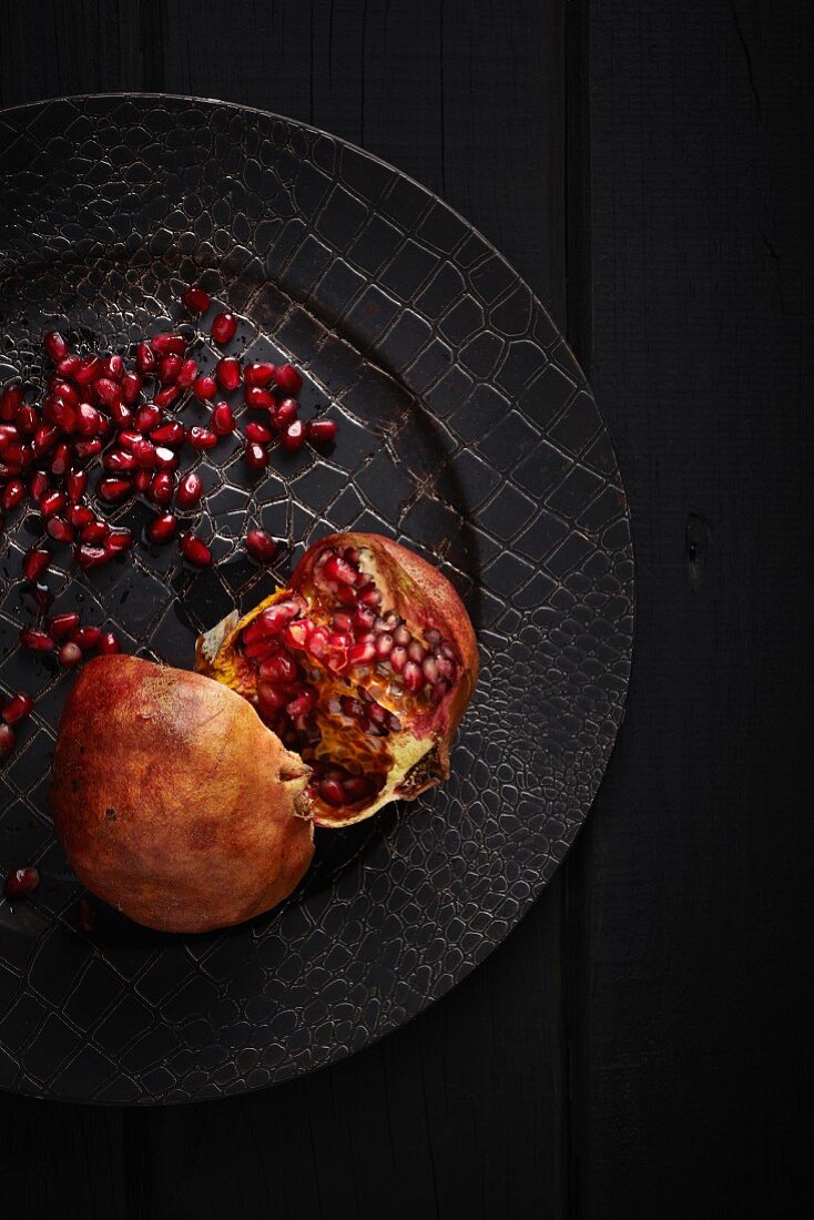 A halved pomegranate on a black plate (seen from above)