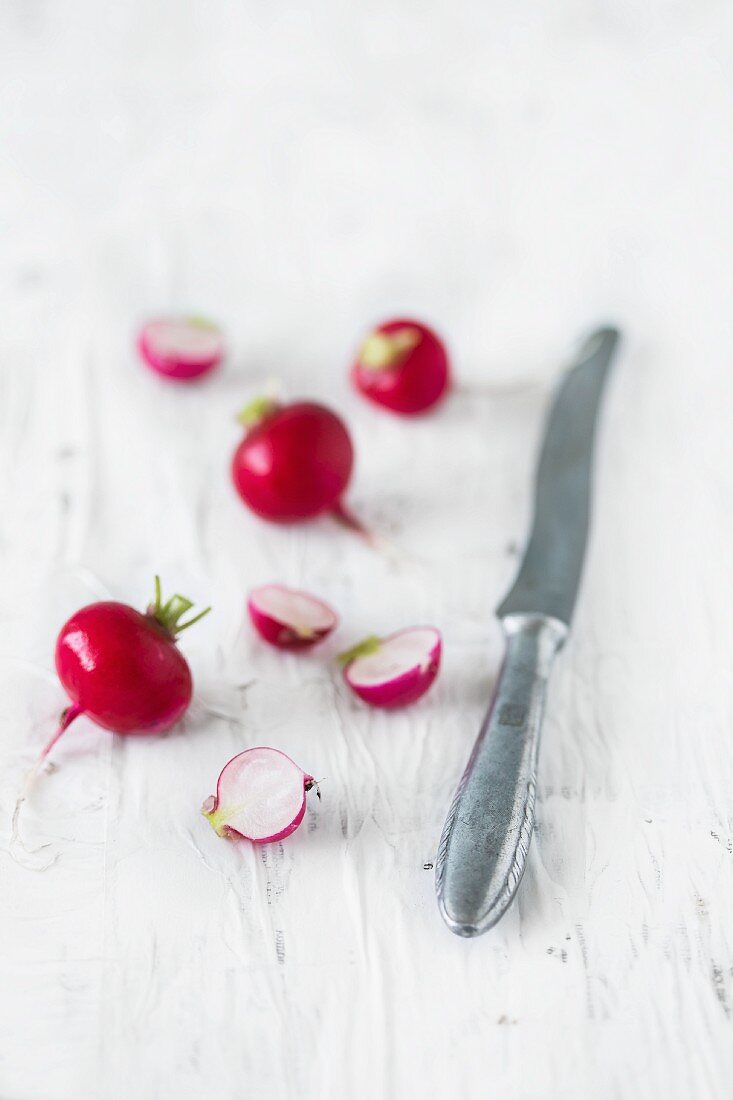 Radishes (whole and halved) on a white wooden surface with a knife