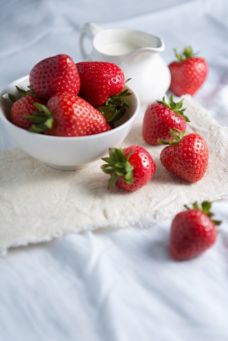 Frische Erdbeeren in einer Schale vor Sahnekännchen auf Leinentuch