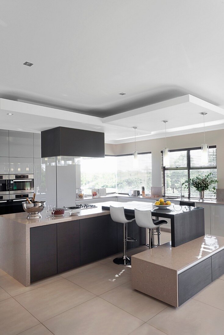 Multifunctional, designer kitchen; breakfast bar with bar stools, attached low sideboard and pendant lamps hanging from suspended ceiling elements