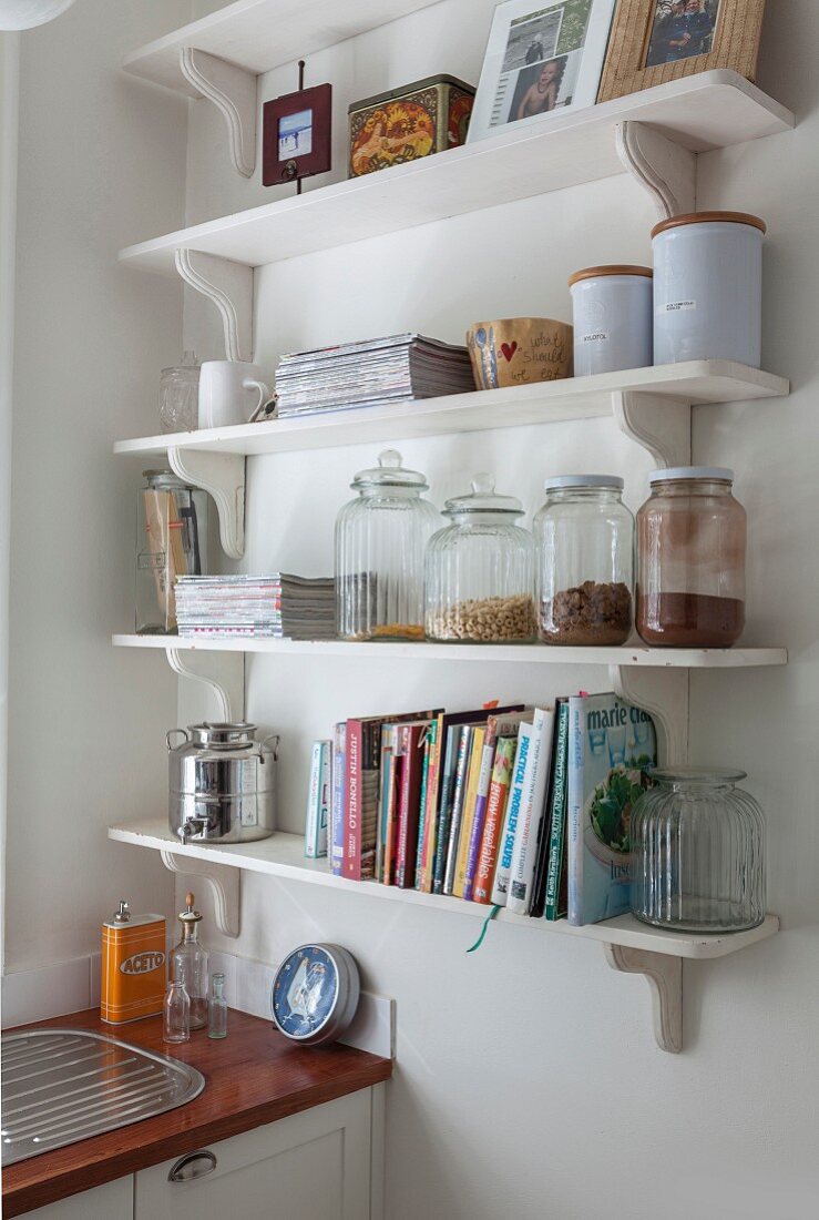 White bracket shelves of storage jars and cookery books in corner of kitchen