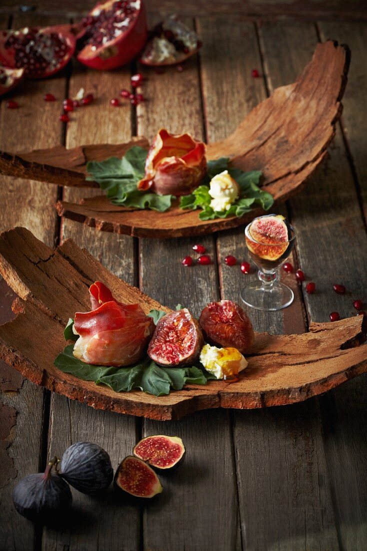 Appetisers with figs, pomegranate seeds, ham and cheese served on pieces of bark