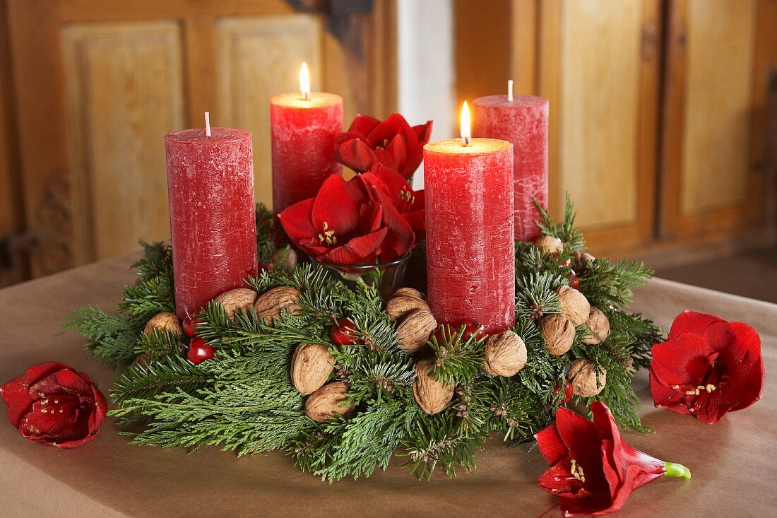 Classic Advent wreath with branches or fir and thuja, walnuts, amaryllis flowers and red candles