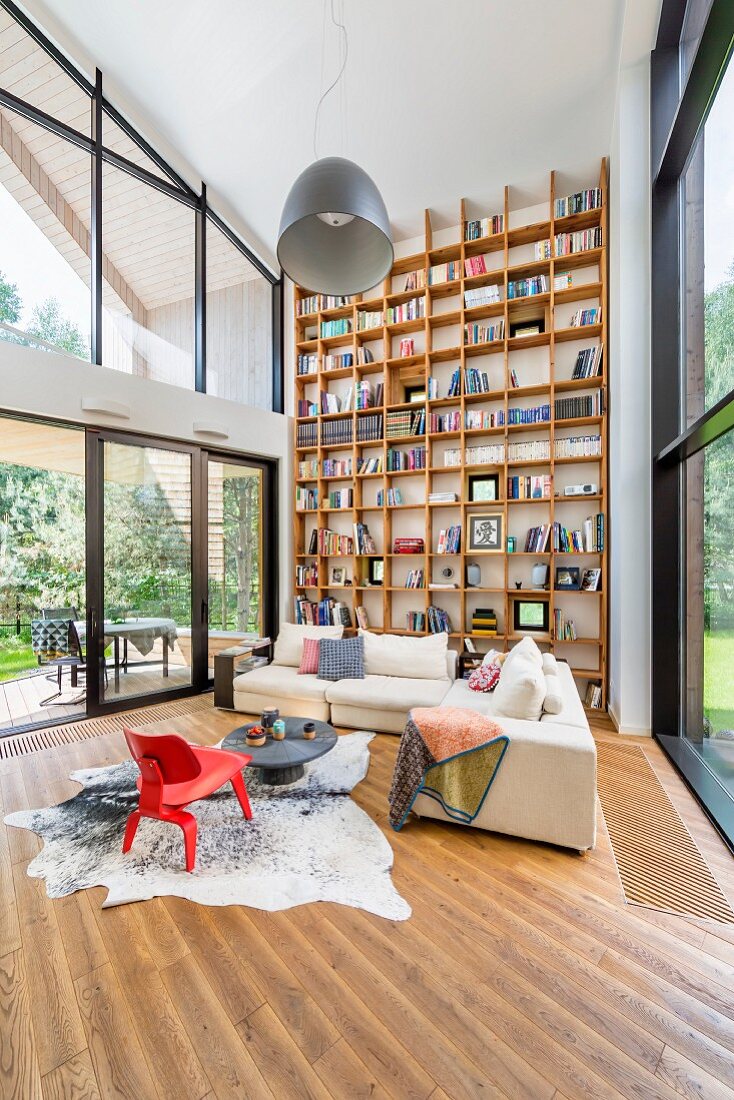 Red classic armchair on animal-skin rug and pale corner sofa in contemporary building with floor-to-ceiling bookcases on one wall