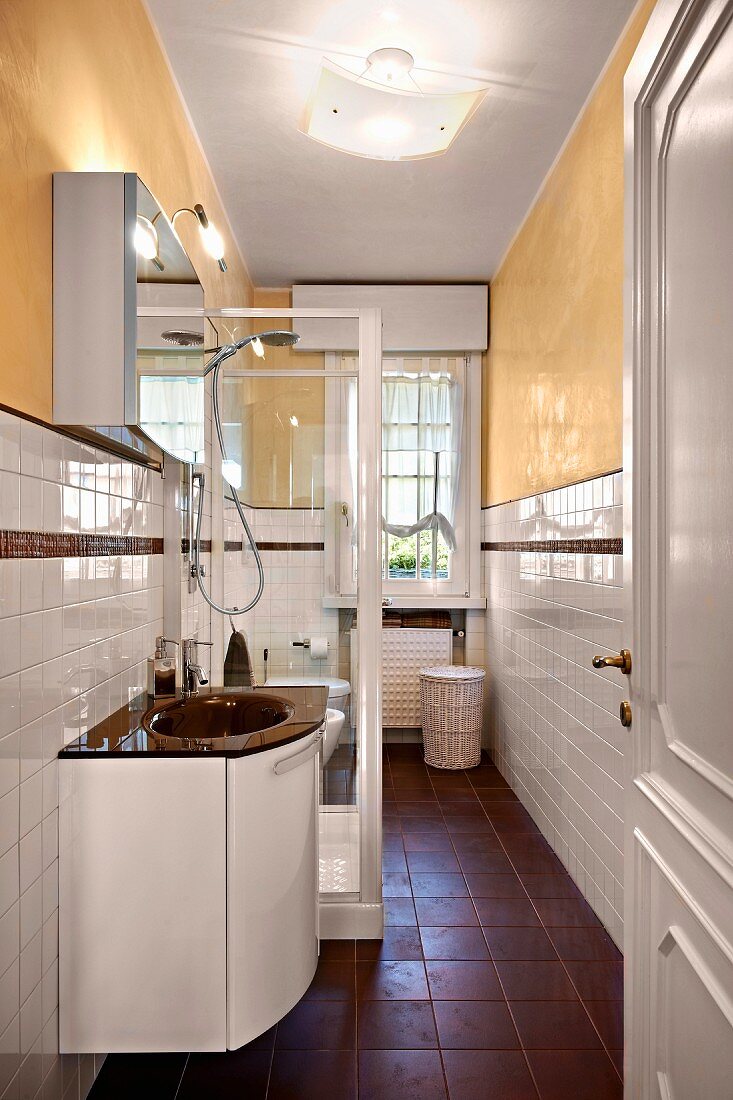 Washstand next to glass shower cabinet in narrow bathroom with yellow-painted walls and white-tiled dado