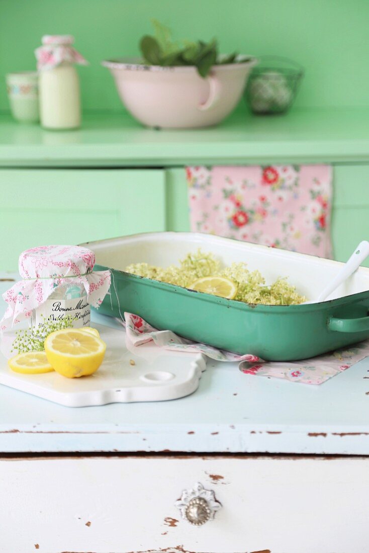 Elderflowers and lemons in green oven dish on white, vintage cabinet