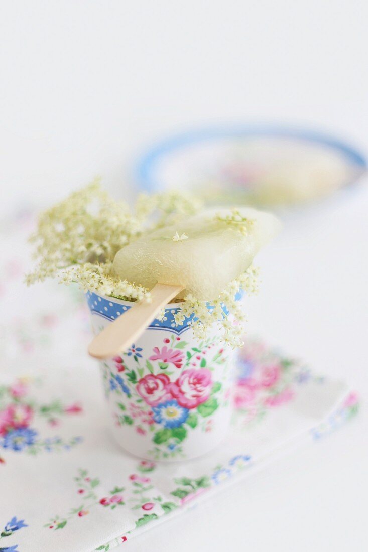 Home-made elderflower ice lilly lying across floral beaker