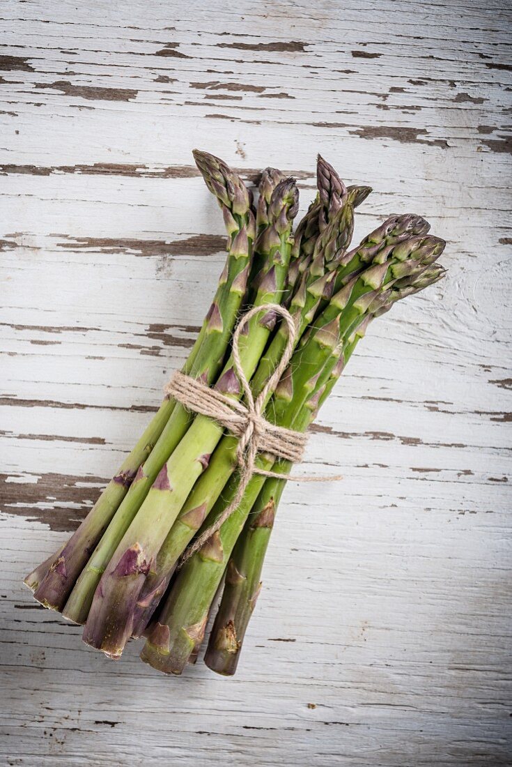 A bundle of asparagus on a white wooden surface