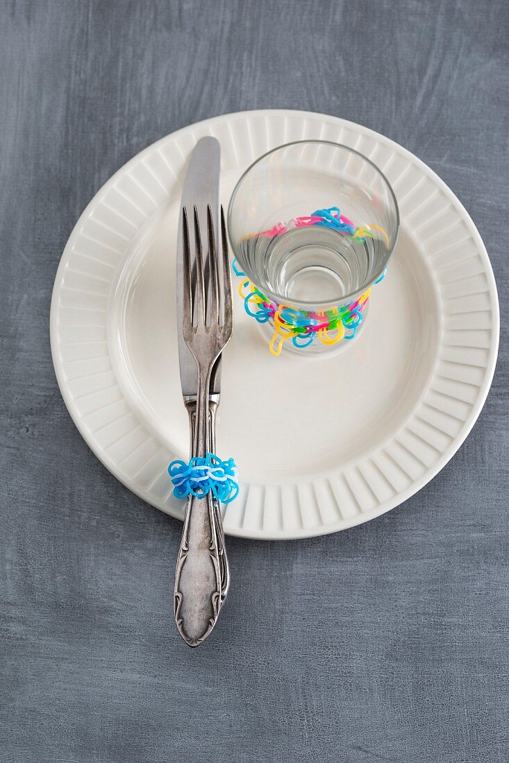 Silver cutlery and a glass decorated with rubber bands on a plate