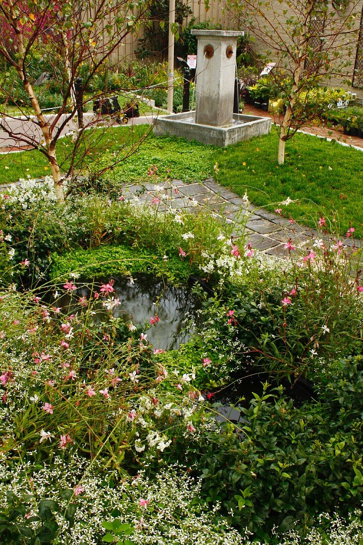 Stone fountain and small, densely planted pond next to garden path