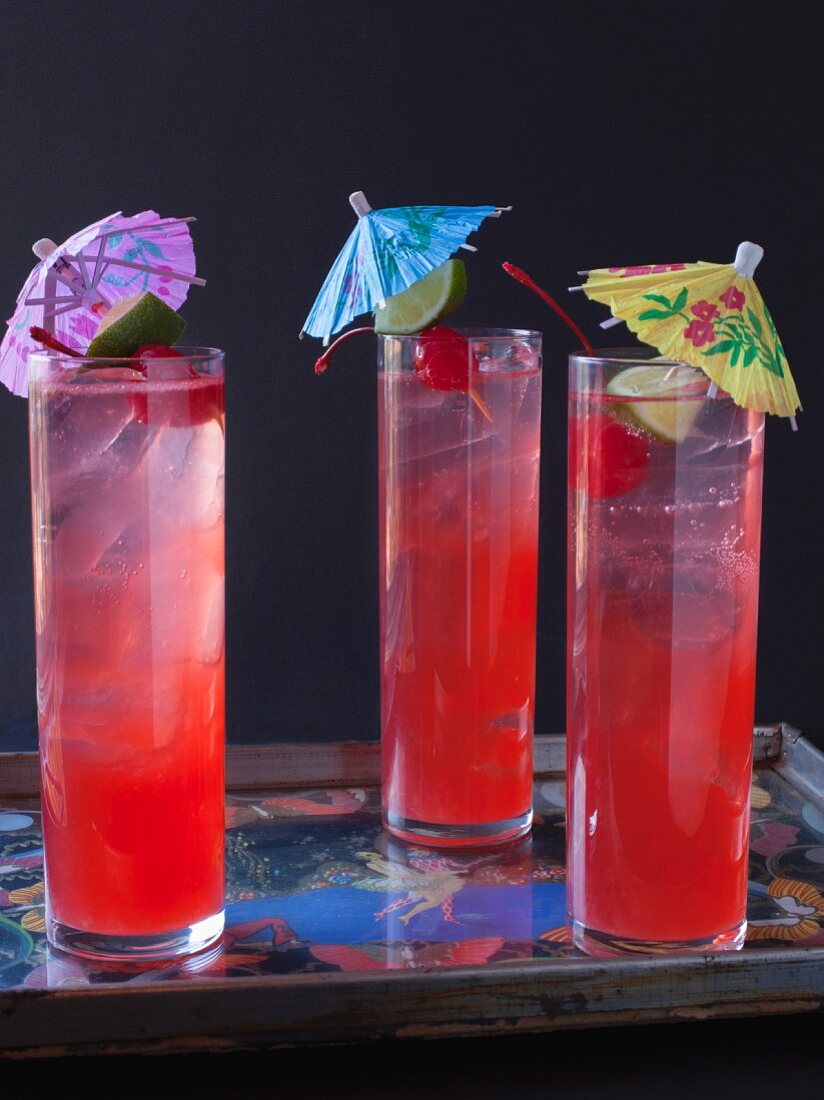 Three Singapore Slings with cocktail umbrellas on a tray