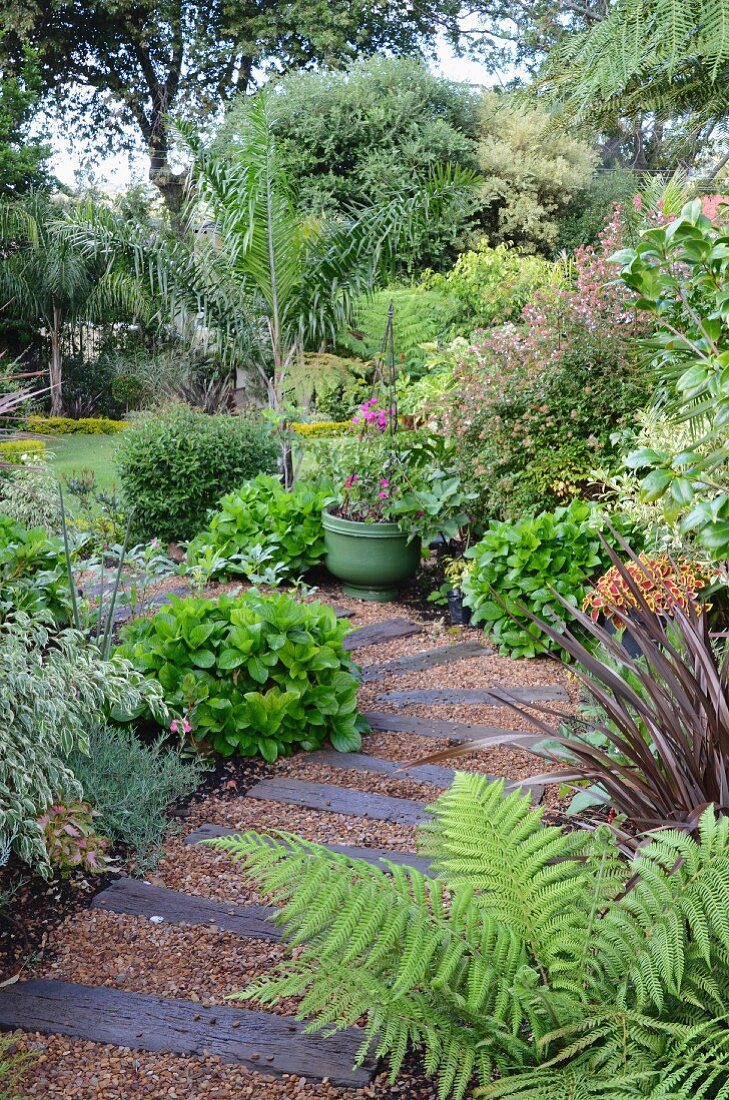 Garden path made from gravel & old railway sleepers in densely planted garden