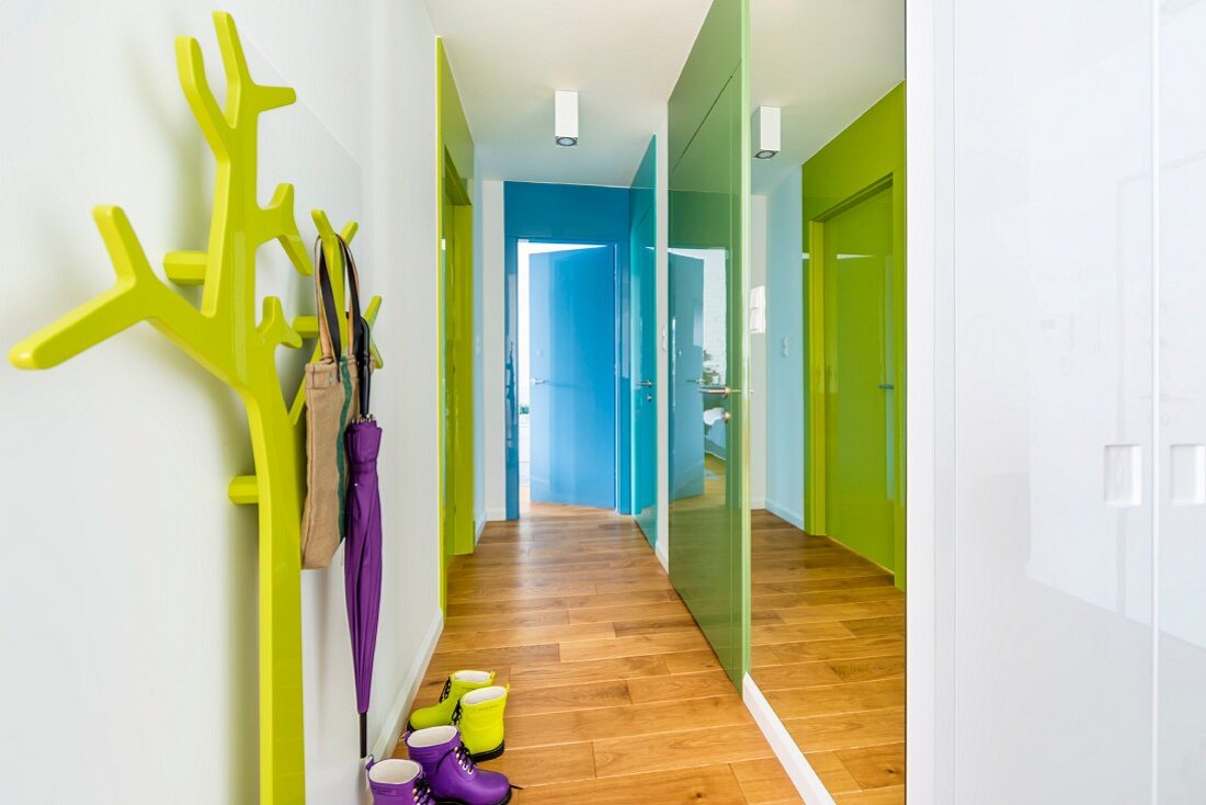 Hallway with mirrored wall, colourful doors and green stylised tree as coat stand