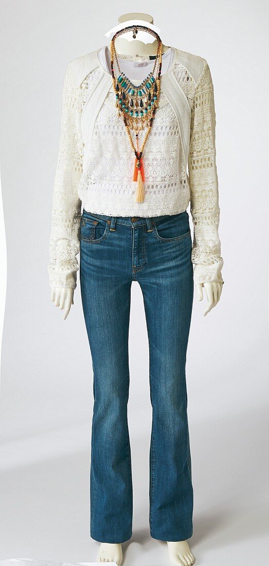 A hippie outfit consisting of jeans, a lace jumper and a necklace on a mannequin