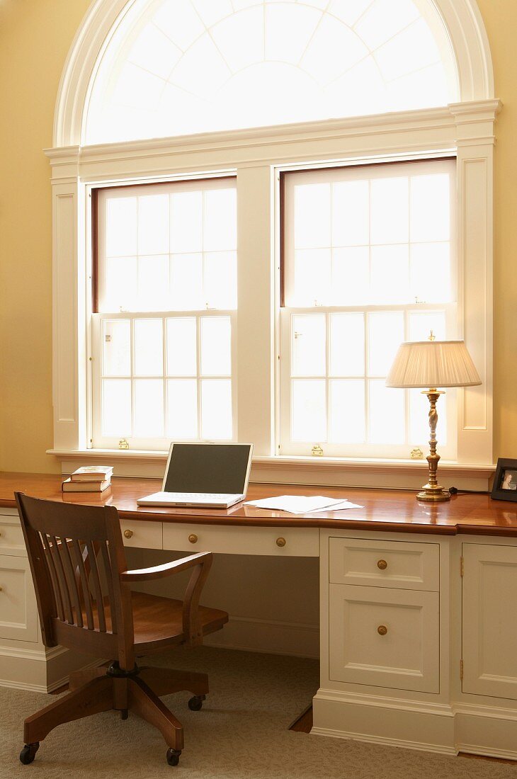 Laptop on traditional desk below large arched window