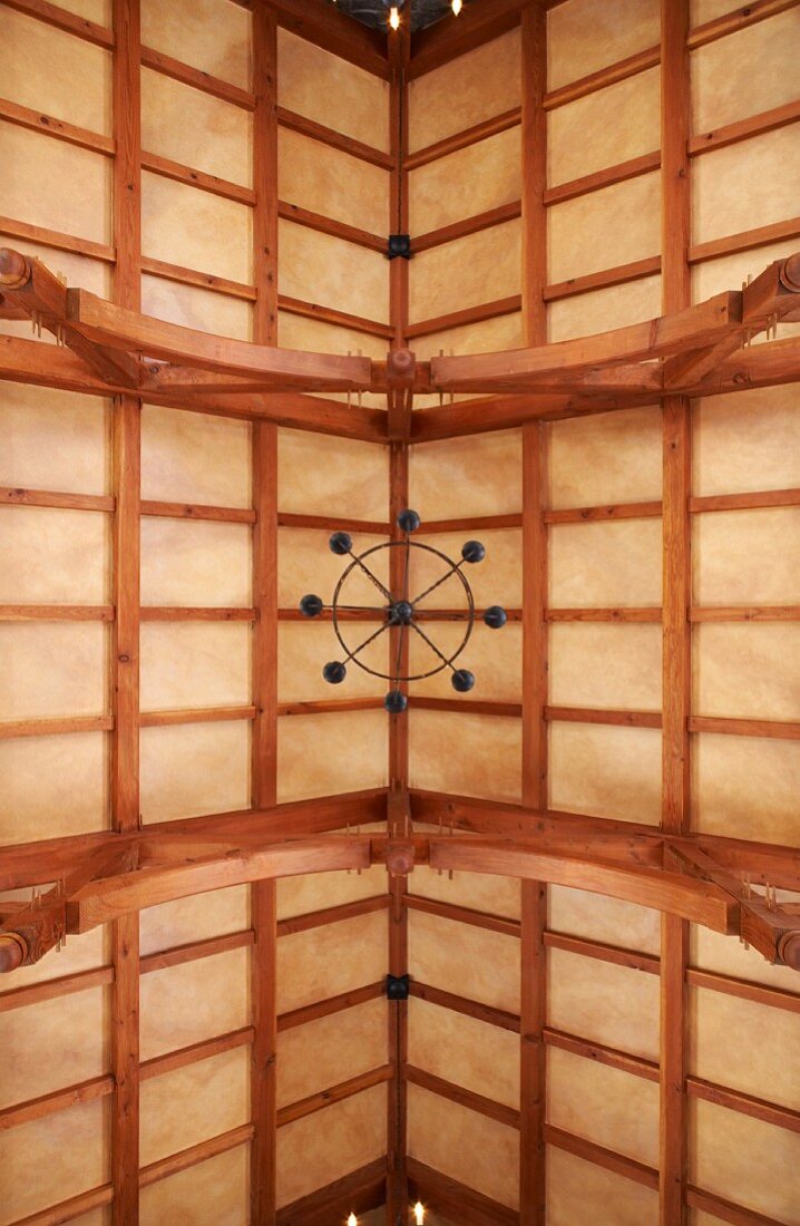 Blick von unten in offene Holzbalkendachkonstruktion mit Kronleuchter eines eleganten Landhauses