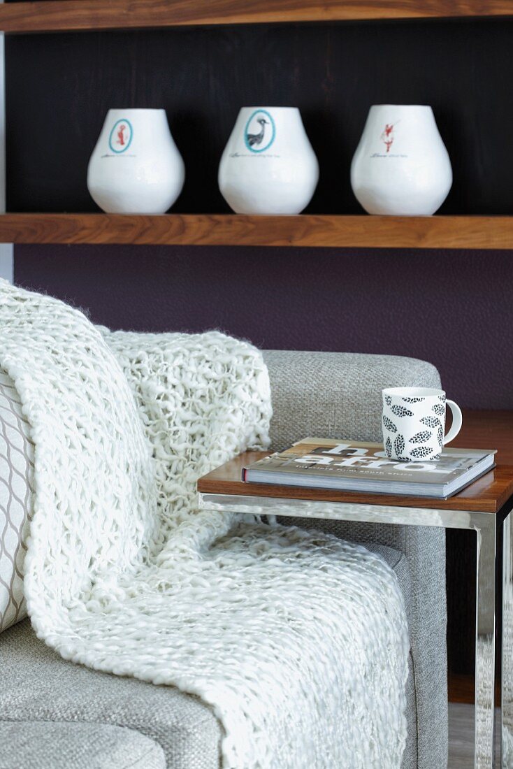 Minimalist side table next to couch in front of vases on wooden shelf