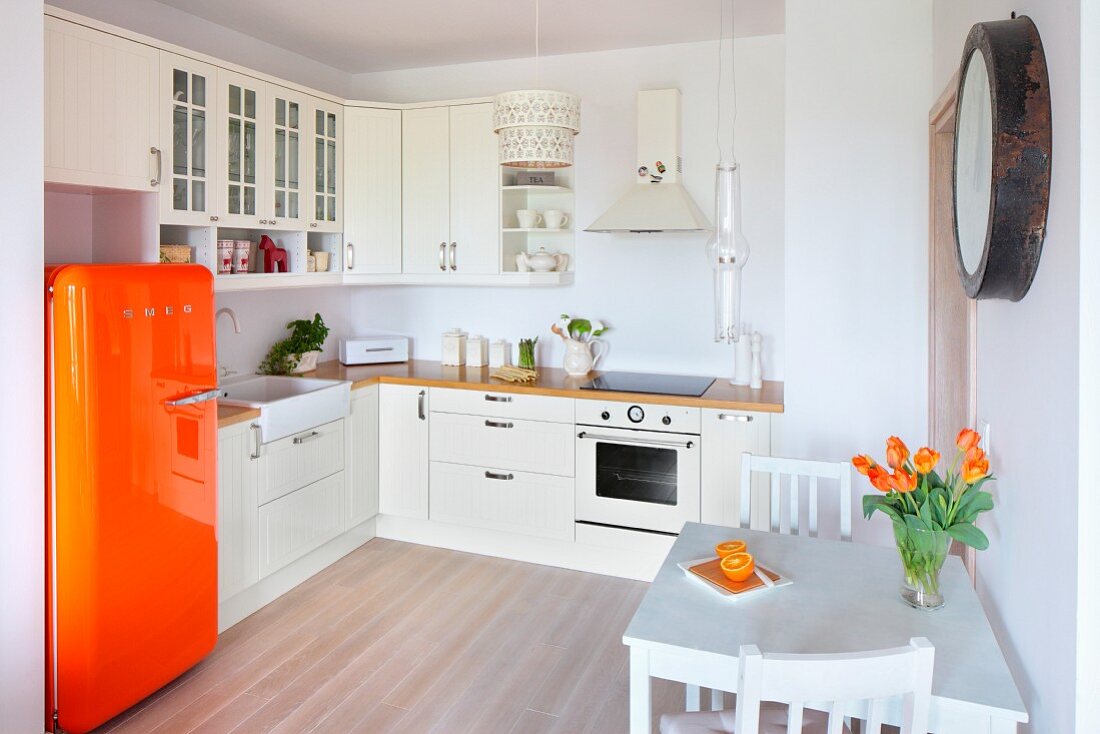 weiße, offene Einbauküche mit orangefarbenem Retro-Kühlschrank und kleinem Essplatz