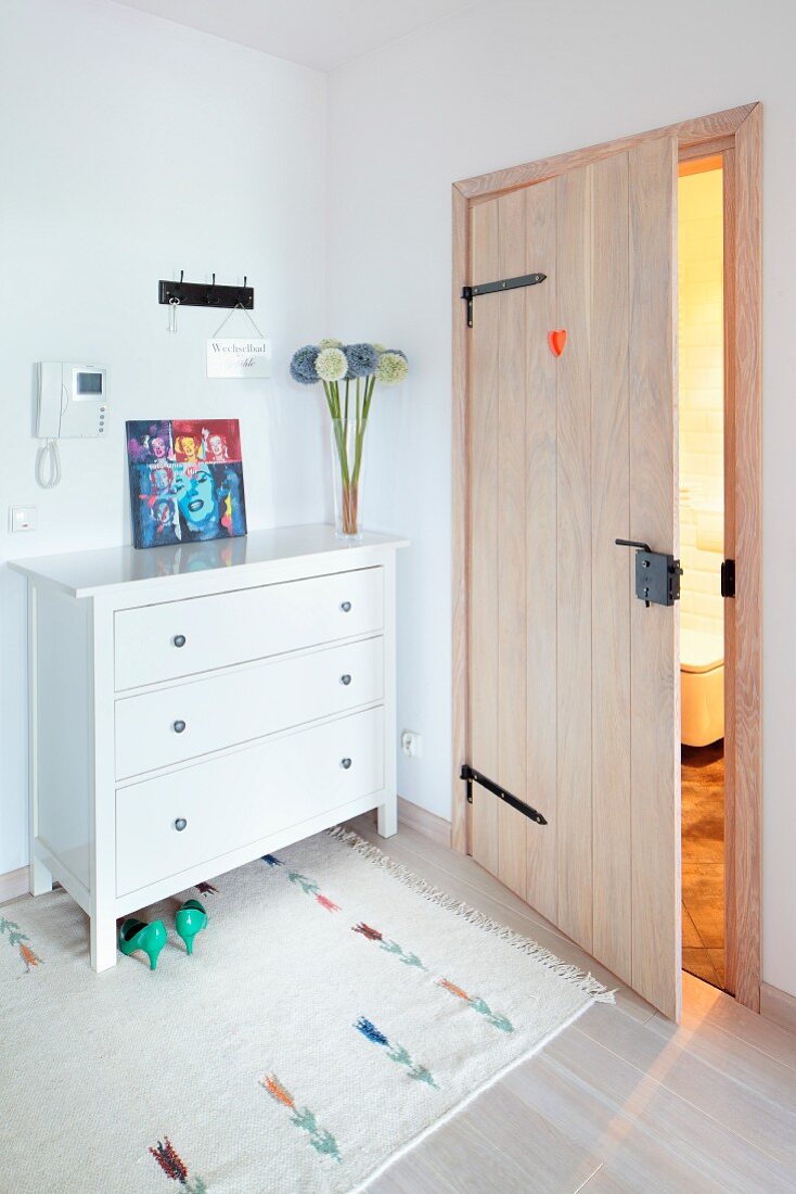 Board door with wrought iron fittings next to white chest of drawers in hall