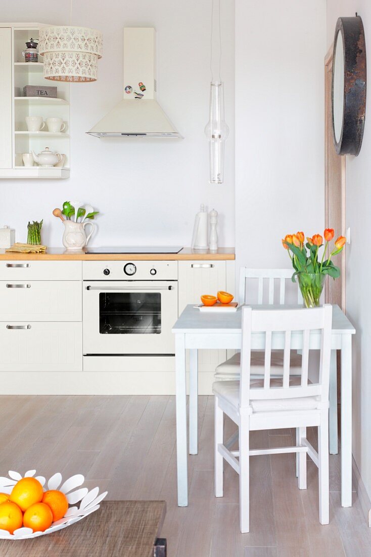 Small dining area with vase of tulips in open-plan kitchen; bowl of oranges on coffee table in foreground