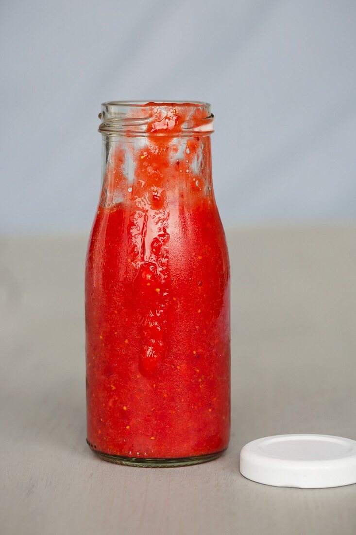 A bottle of strawberry sauce with a lid