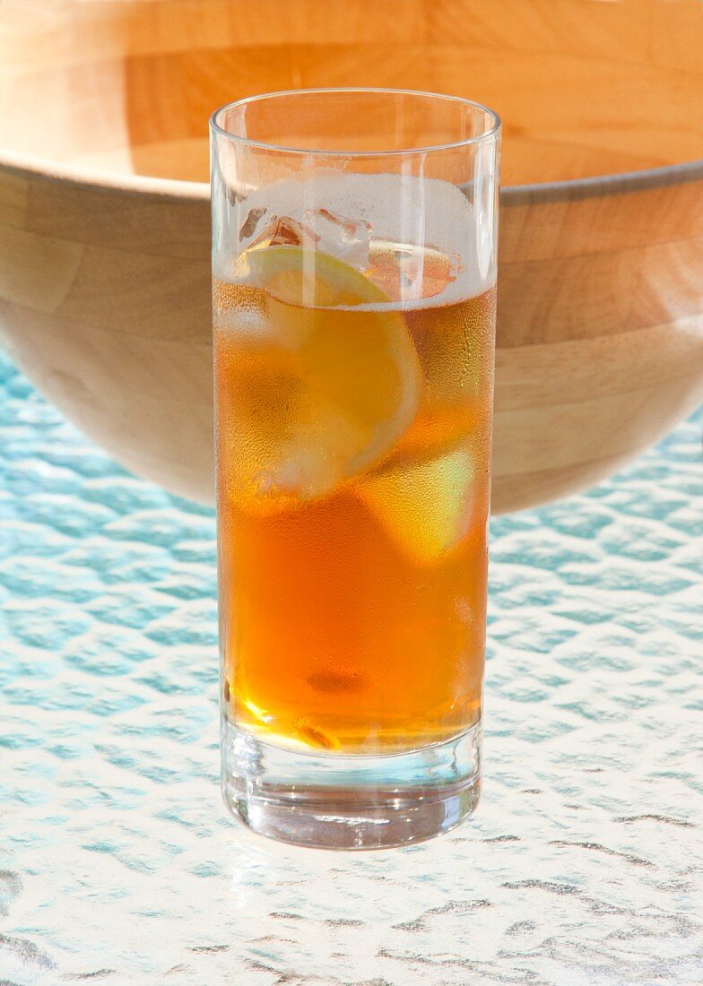 Pimms with soda and lemon with a wooden bowl behind it