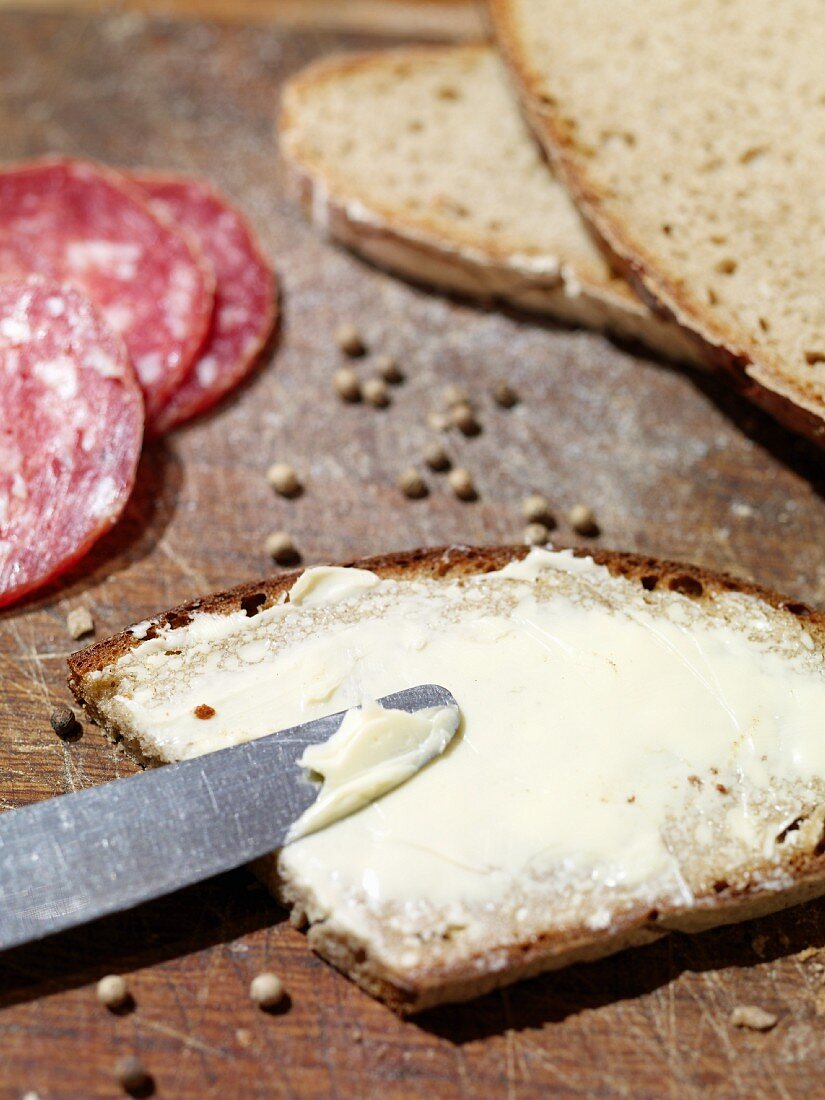 A slice of rye bread spread with butter with salami and peppercorns