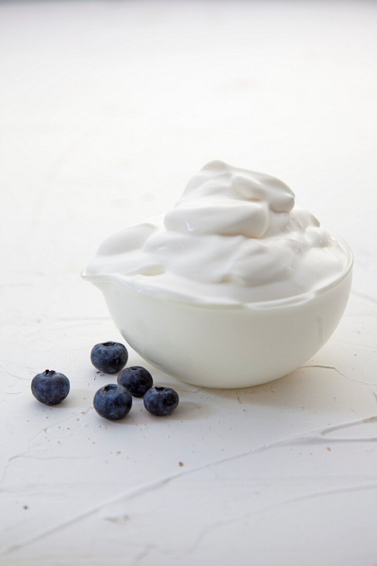 A bowl of whipped cream with fresh blueberries next to it