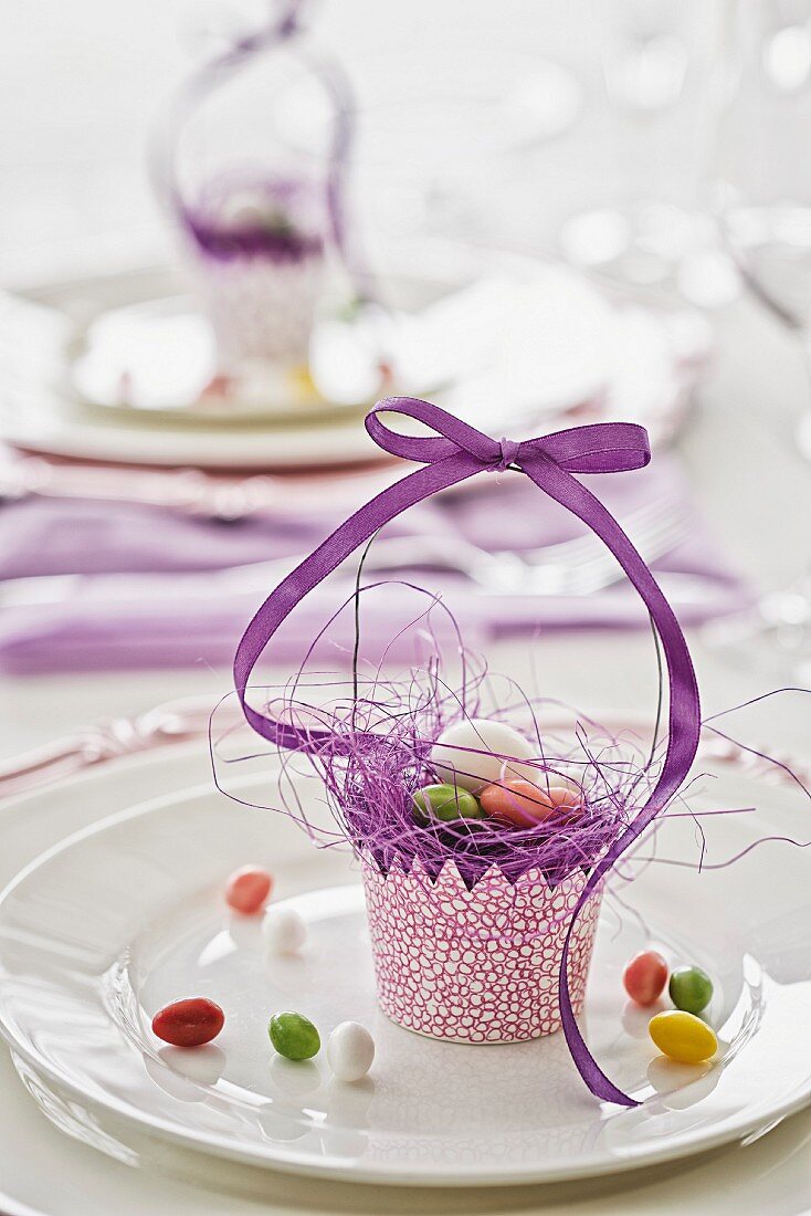 Festliche österliche Tischdekoration mit selbst gebasteltem Papierkörbchen und lila Geschenkband