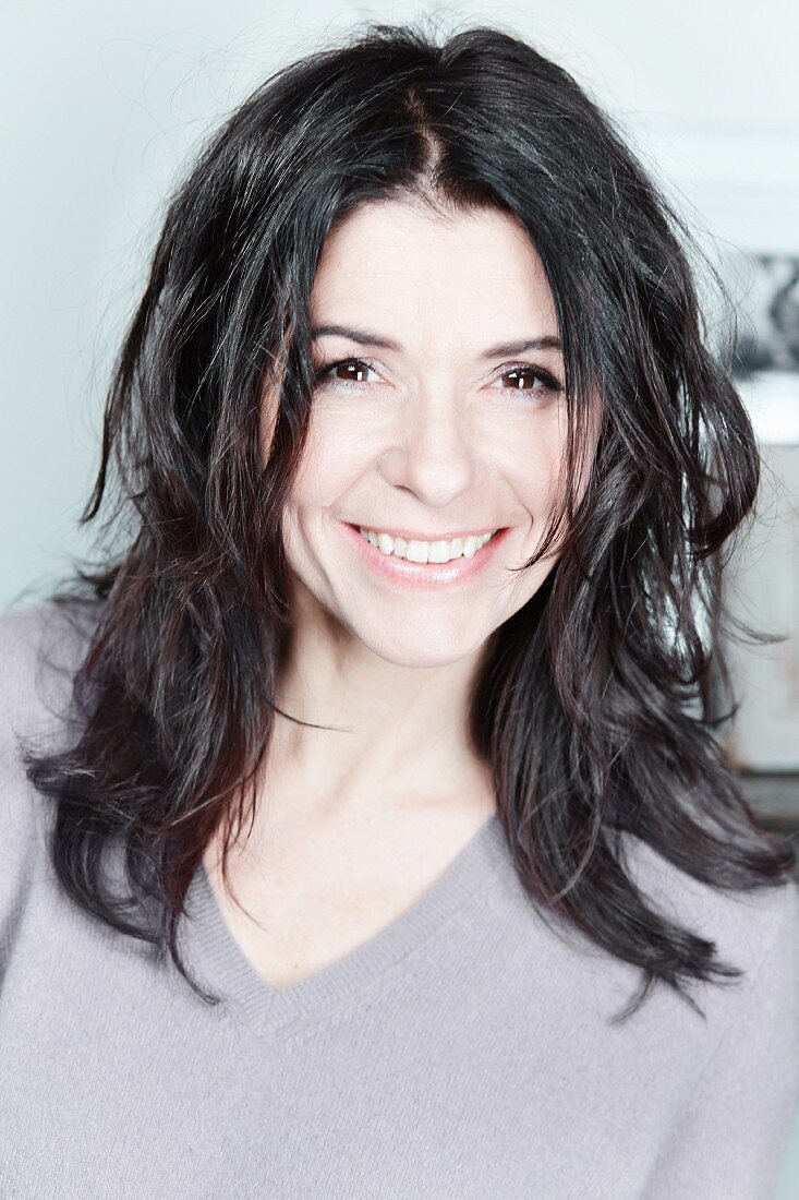 A smiling middle-aged woman wearing a grey cashmere jumper