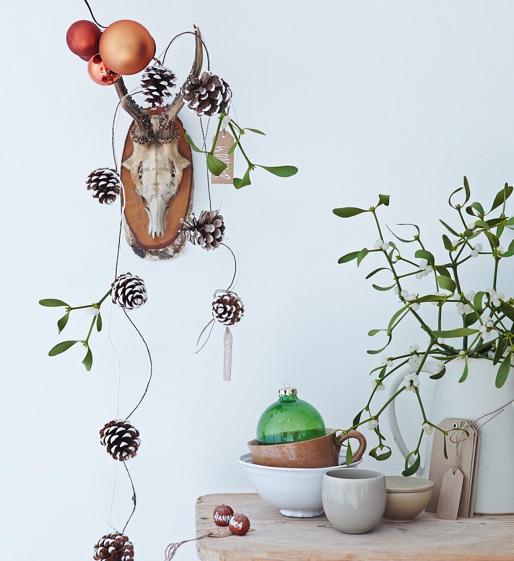 Hunting trophy decorated with garland of pine cones and baubles, stoneware crockery and sprig of mistletoe