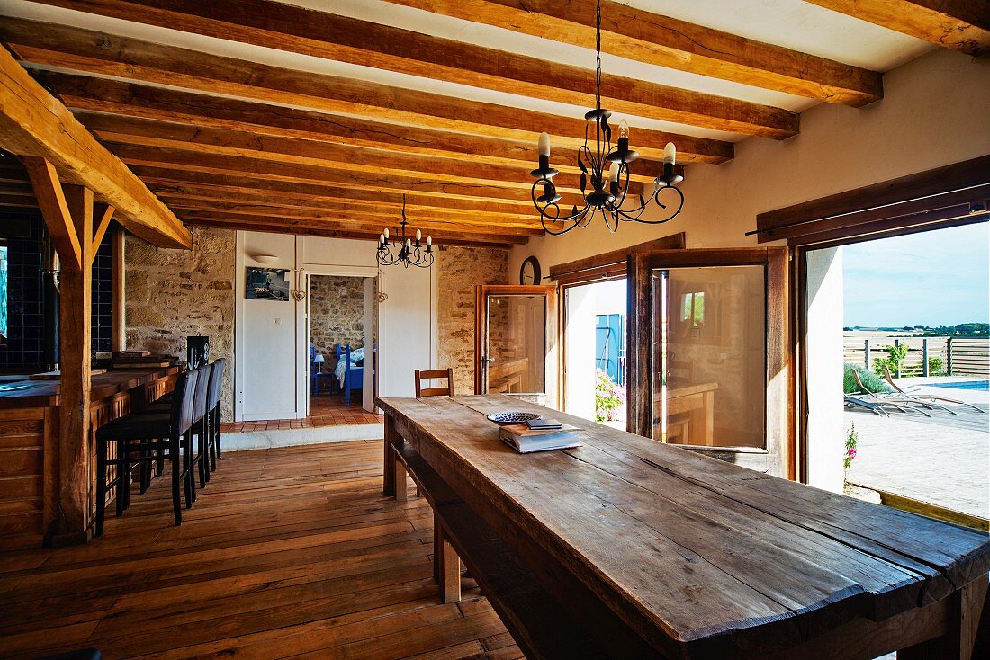 Long wooden table and terrace doors in open-plan kitchen with wood-beamed ceiling in Mediterranean country house