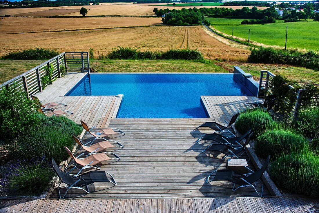Sun loungers and large lavender bushes on wooden terrace with integrated pool and view over landscape of fields