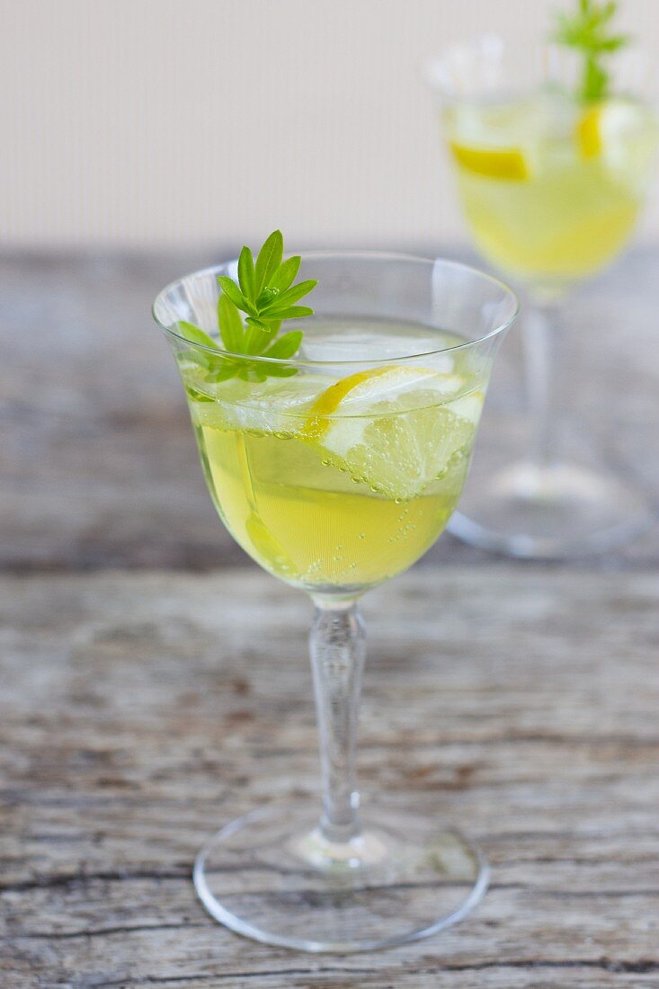 A glass of woodruff punch with ice cubes, lemon and woodruff