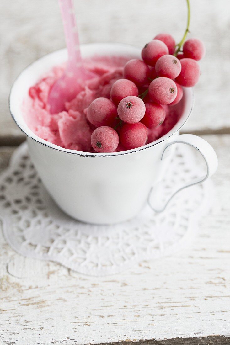 Creamy redcurrant ice cream in a white cup with a frozen sprig of redcurrants