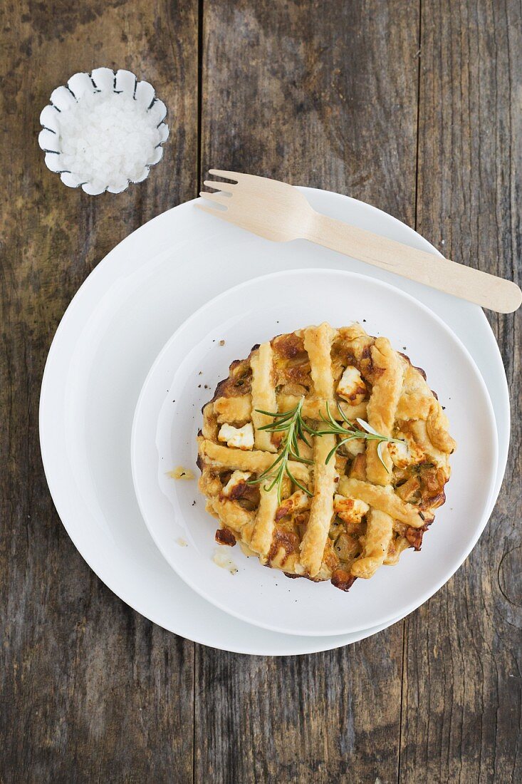 A mini quiche with apples, rosemary and sheep's cheese on a white plate with sea salt