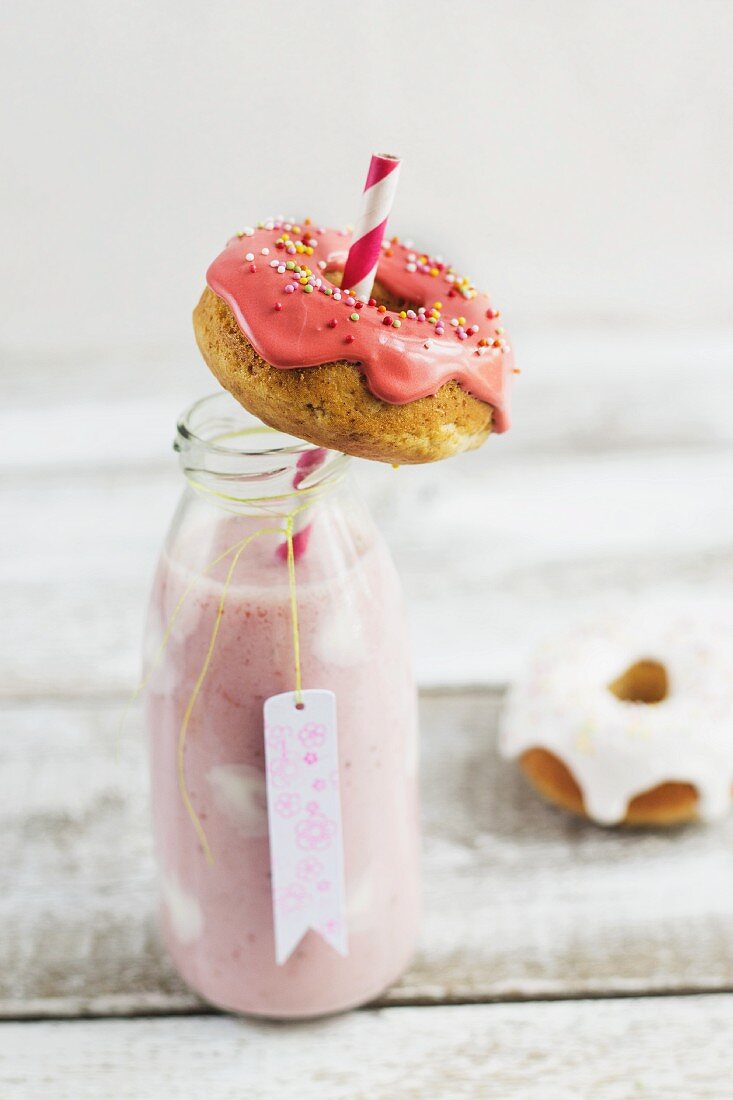A bottle of strawberry milk shake dotted with yoghurt and mini iced doughnuts