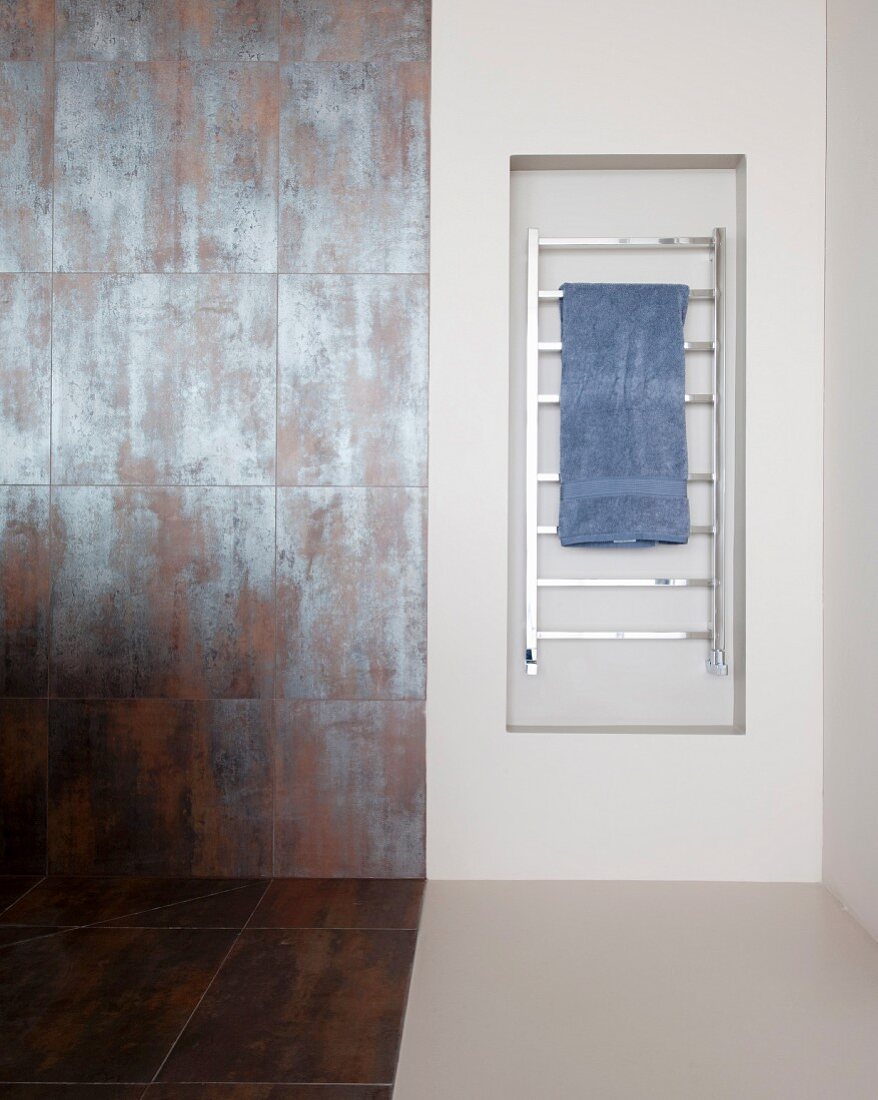 Heated towel rail in niche next to rust-effect tiles