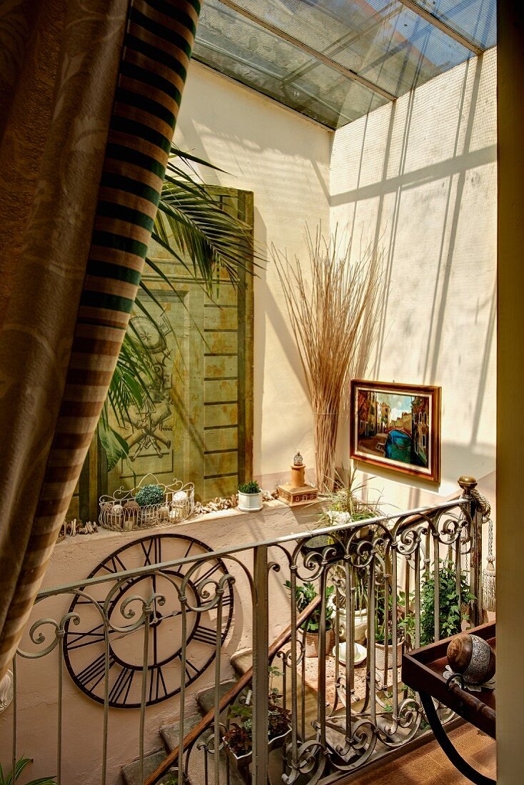 Sunlight falling through skylight into Mediterranean stairwell with wrought iron balustrade and jumble of ornaments on windowsill