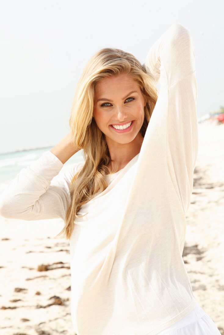 A young blonde woman on a beach wearing a long, white shirt