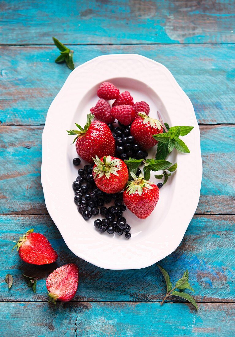 Frische Beeren mit Minzeblättern auf Teller (Aufsicht)