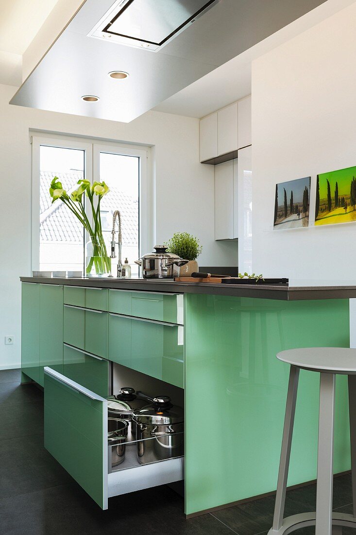 A shiny, mint-coloured designer kitchen bar with an opened drawer and a stainless steel extractor fan