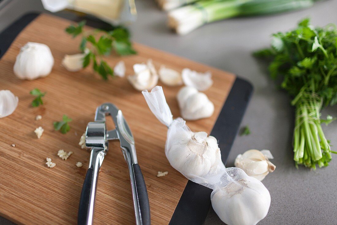 An elegant chopping board with a garlic press, garlic cloves and parsley