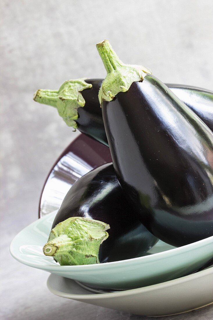 Three fresh, raw aubergines on a stack of plates