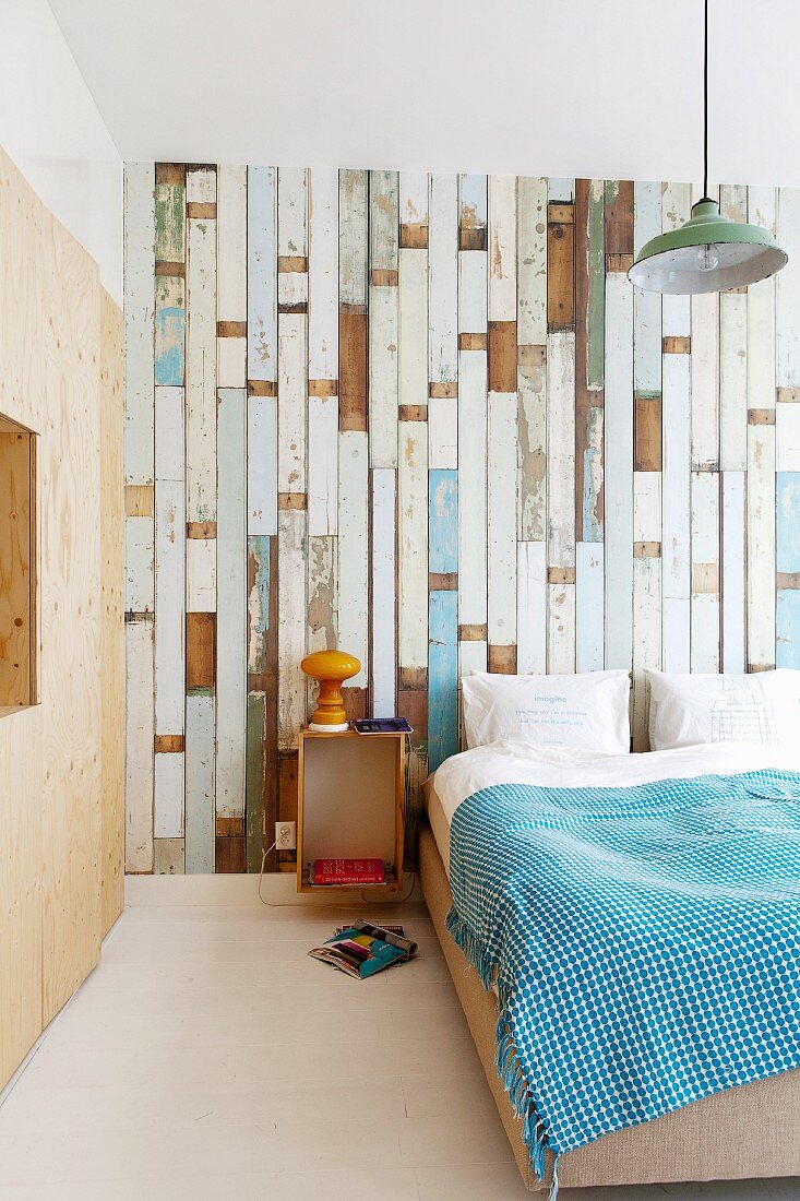 Bed against wallpaper with pattern of old floorboards and plywood fitted wardrobe to one side