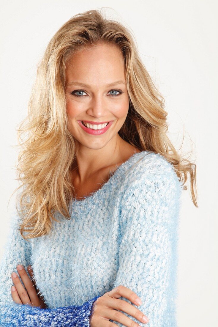 A blonde woman with her arms folded wearing a blue-toned, coarse-knit jumper